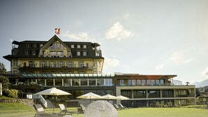 A large hotel with multiple balconies, outdoor seating, and a mountain view. - Belvédère Strandhotel (Spiez)