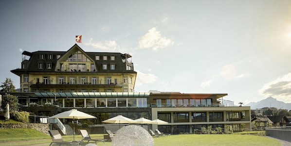 Un hotel grande con varios balcones, mobiliario exterior y vistas a la montaña.