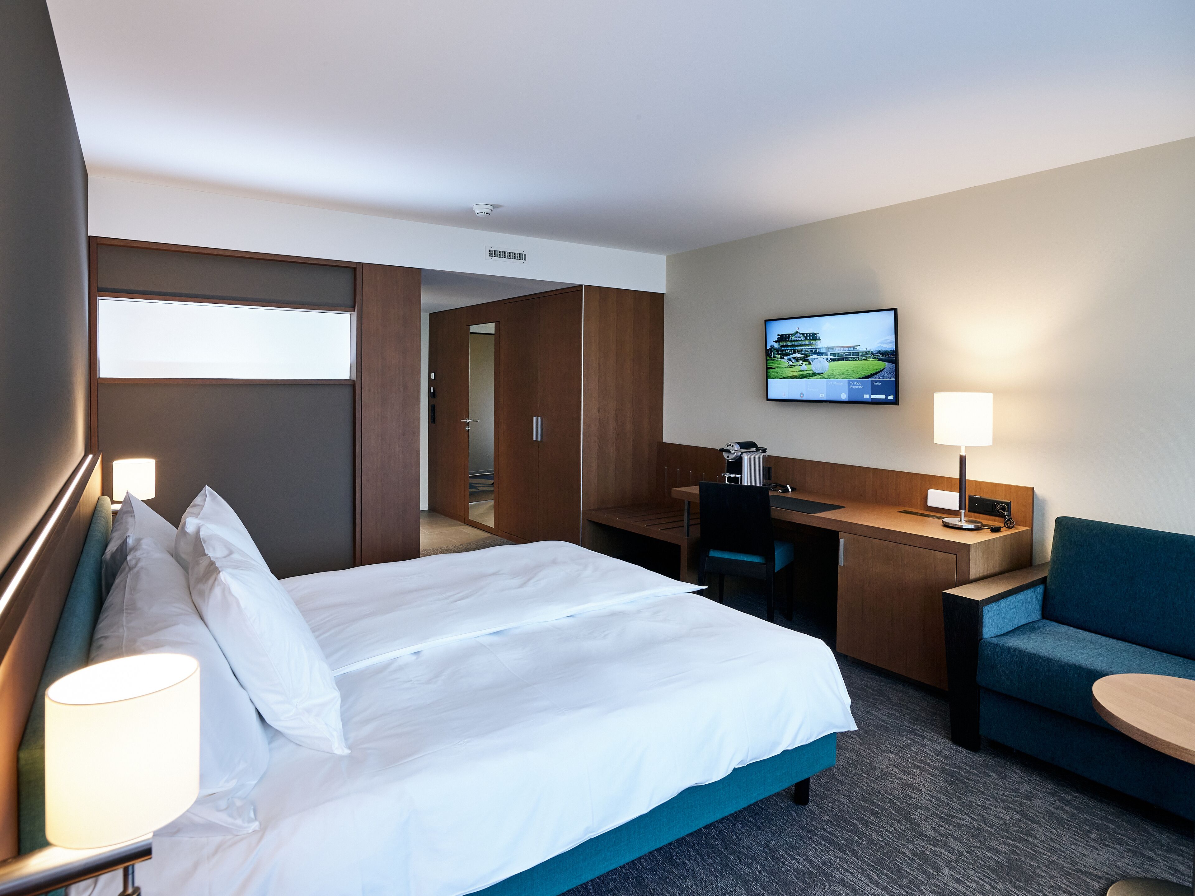 Una habitaci ón de hotel con cama, escritorio, silla, televisión y sofá.