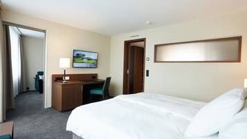 A hotel room with a bed, a desk, a chair, a TV, and a door.