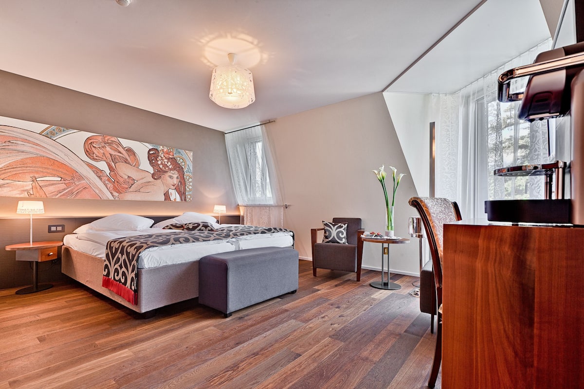 A modern hotel room with a large bed, a desk, a chair, and a dining table.