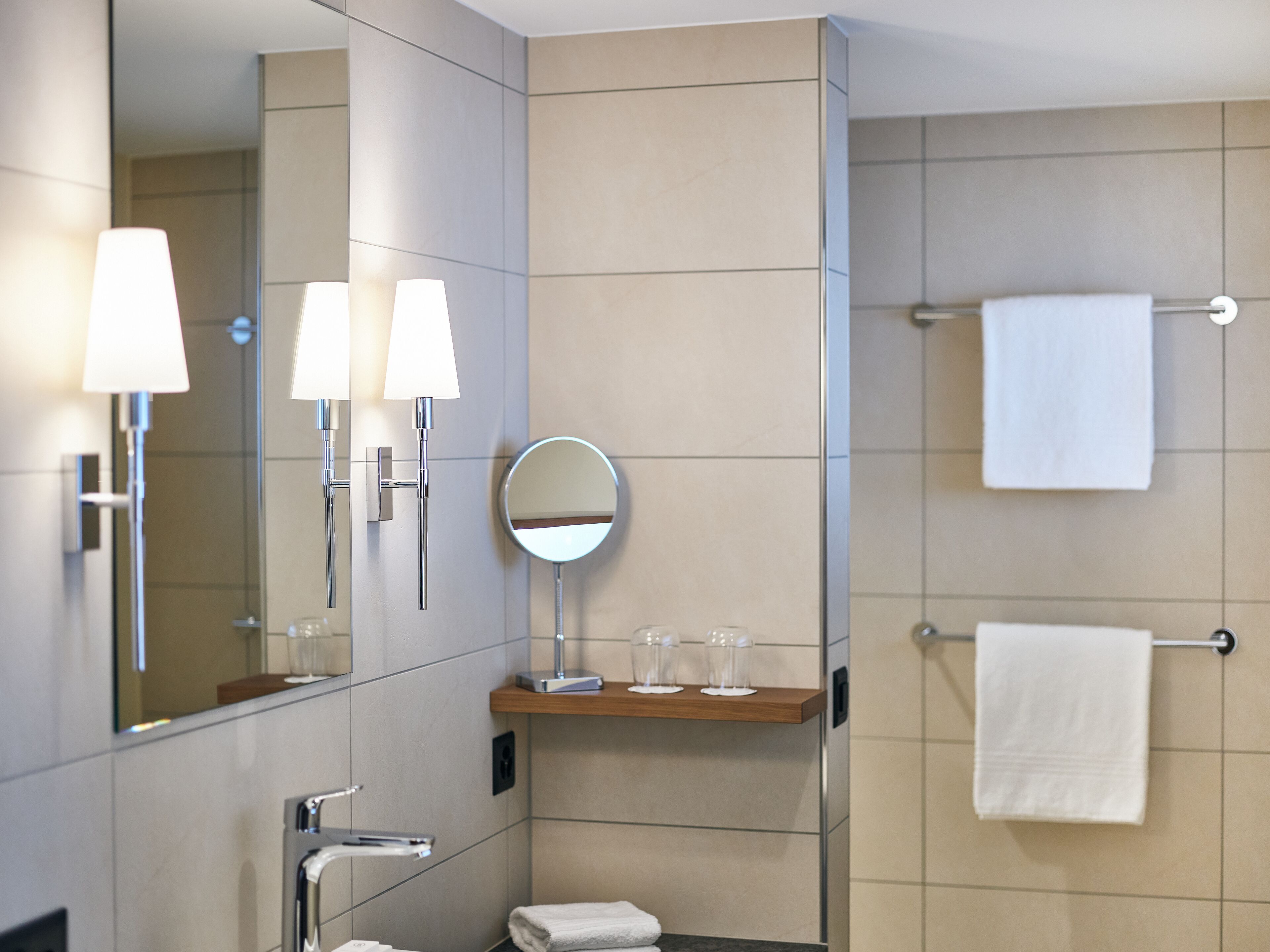 Un baño moderno con un espejo grande, dos luces empotradas, un perchero y una repisa con vasos.