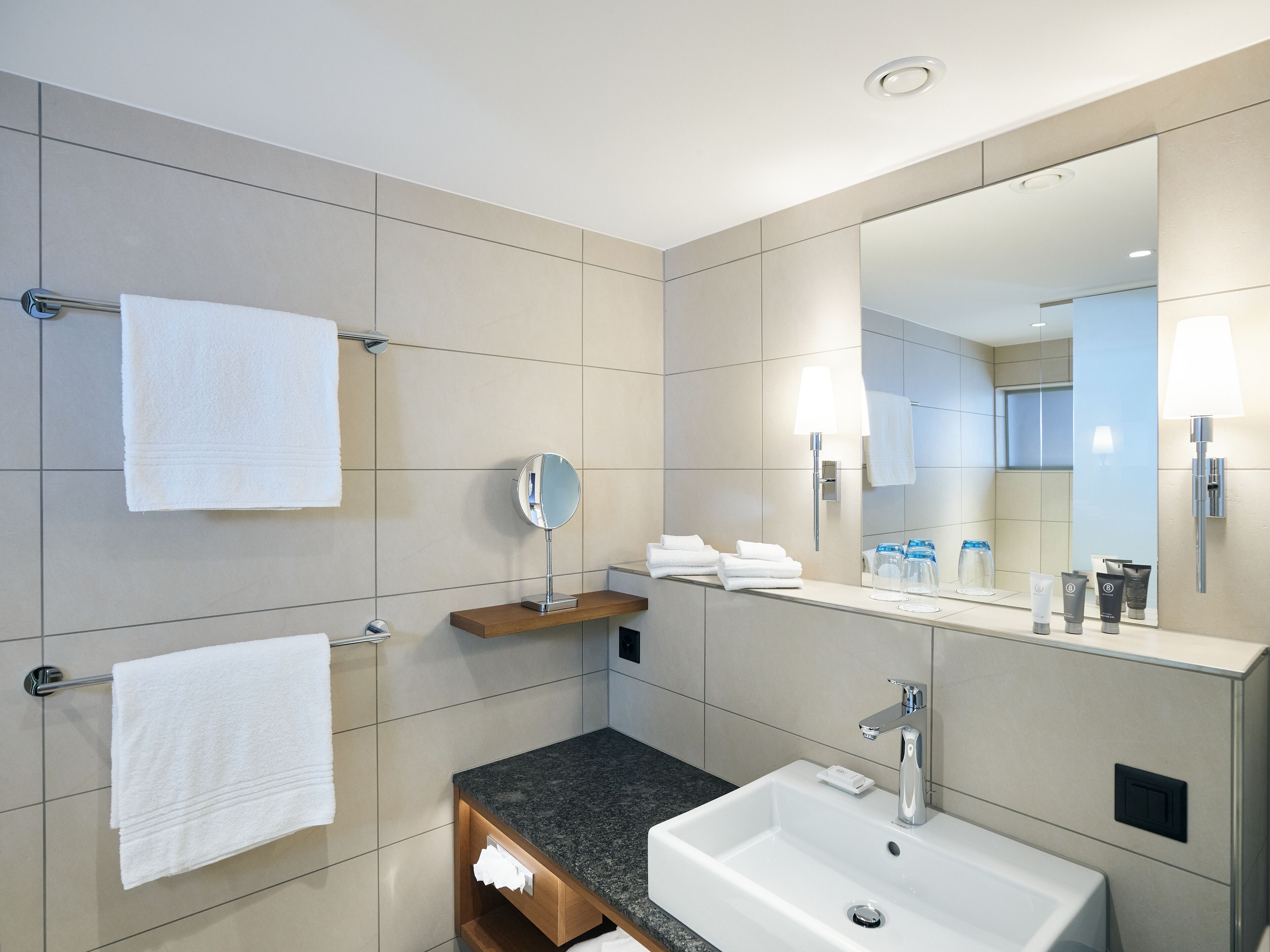 Un baño moderno con un espejo grande, un lavamanos y dos toalleros.