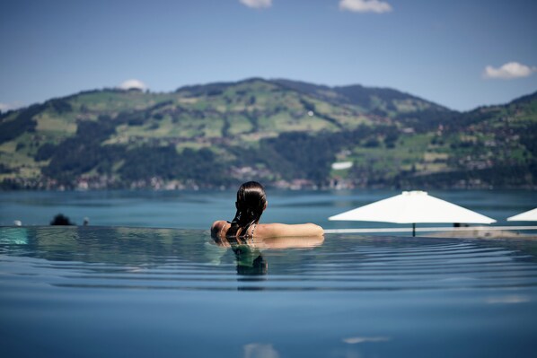 A person relaxing in a clear pool with a mountainous landscape in the background. - Belvédère Strandhotel (Spiez)