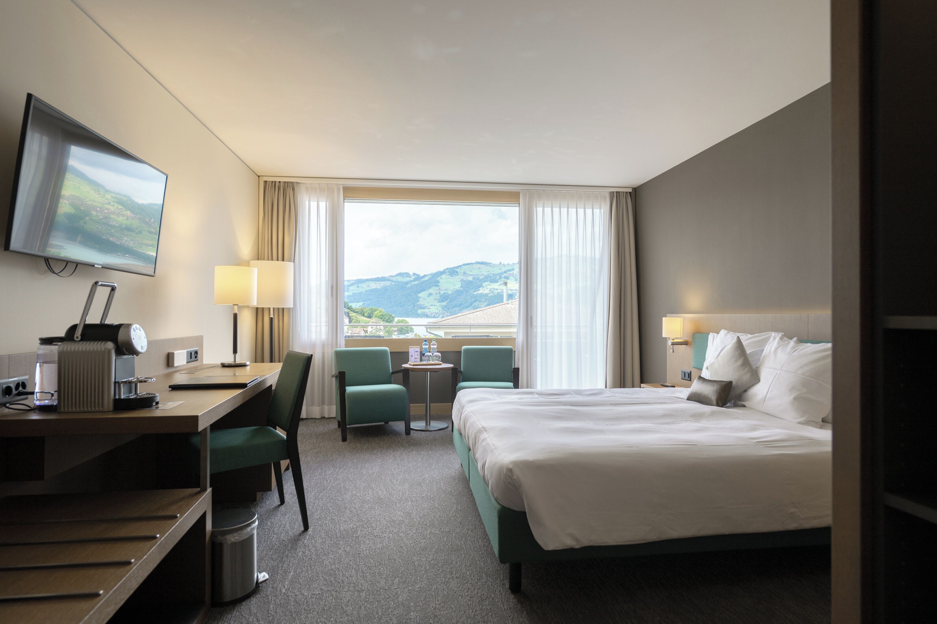 Una habitación de hotel con cama, escritorio, sillas, televisión y vistas a las montañas.