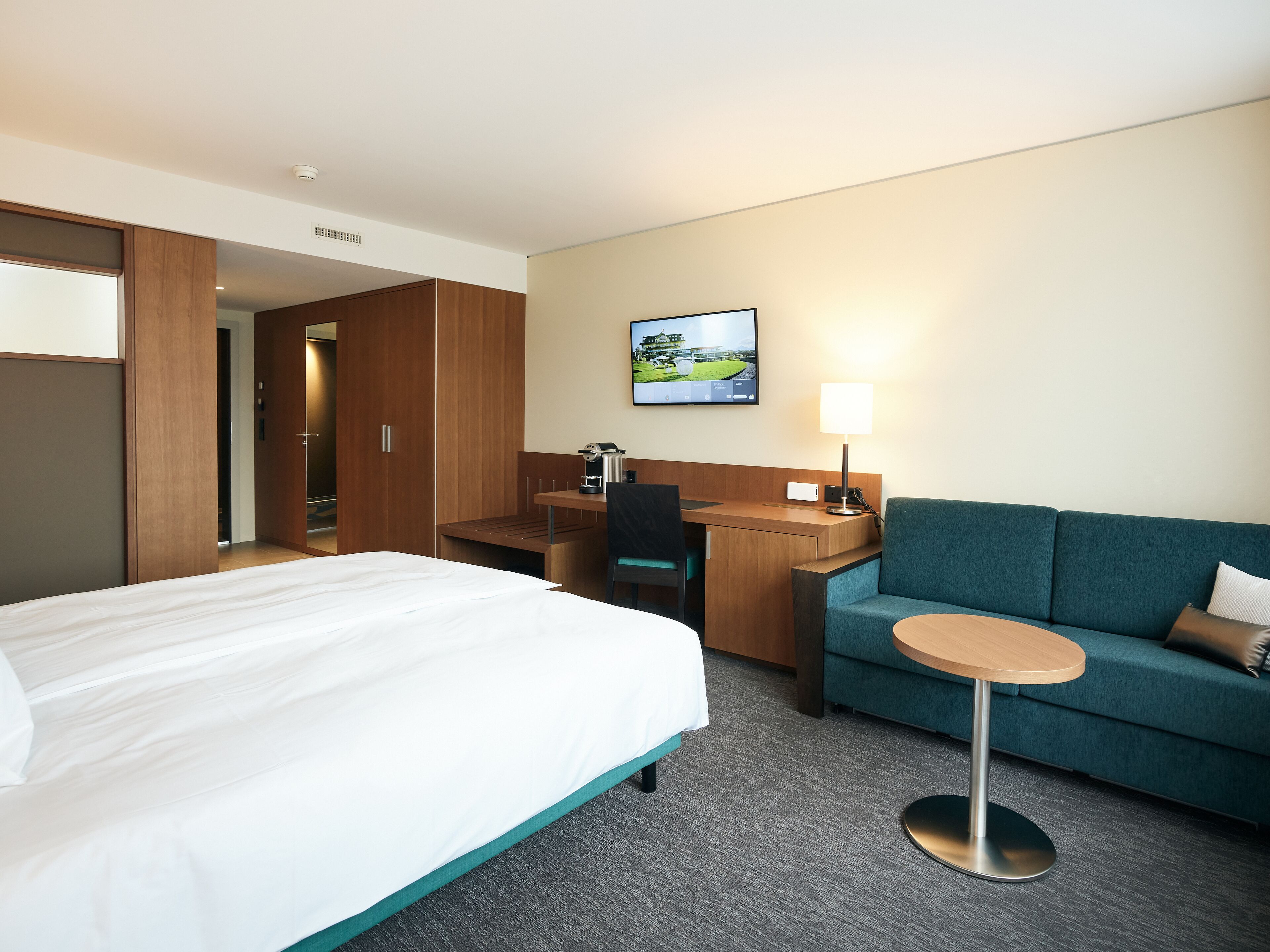A hotel room with a bed, a desk, a chair, a sofa, and a small table.