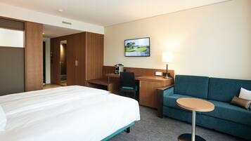 A hotel room with a bed, a desk, a chair, a sofa, and a small table.
