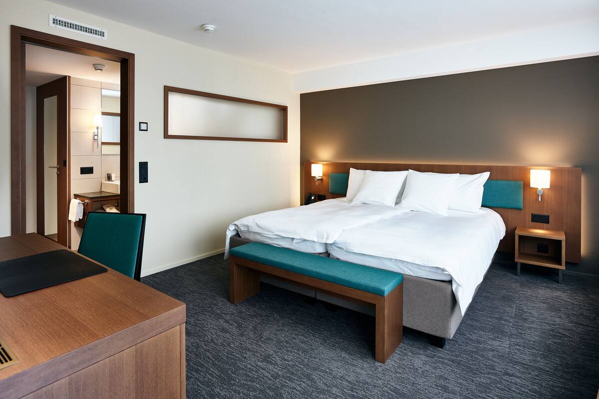 A hotel room with a bed, bedside tables, a desk, and a chair.