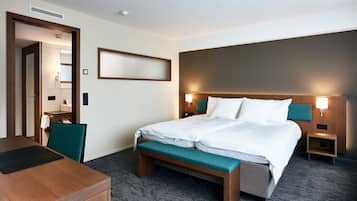 Quarto de hotel com cama, mesas de cabeceira, escrivaninha e uma cadeira.