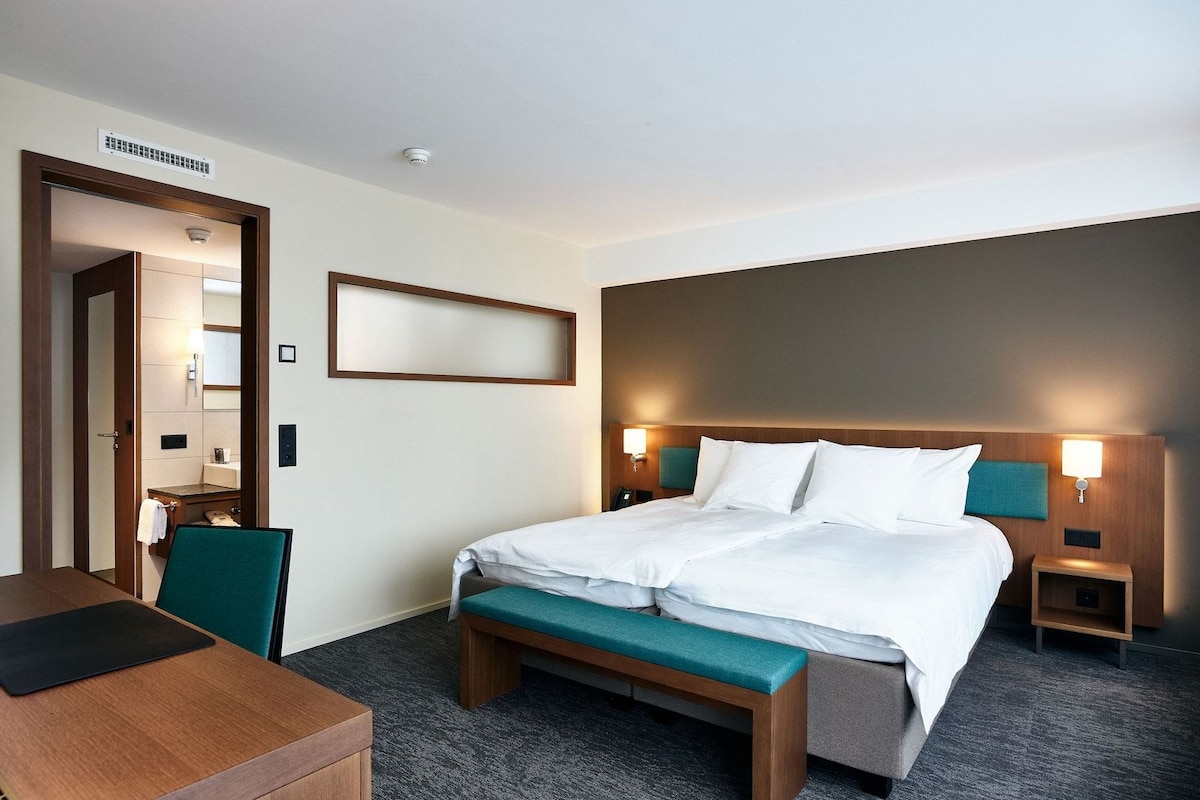 A hotel room with a bed, bedside tables, a desk, and a mirror.