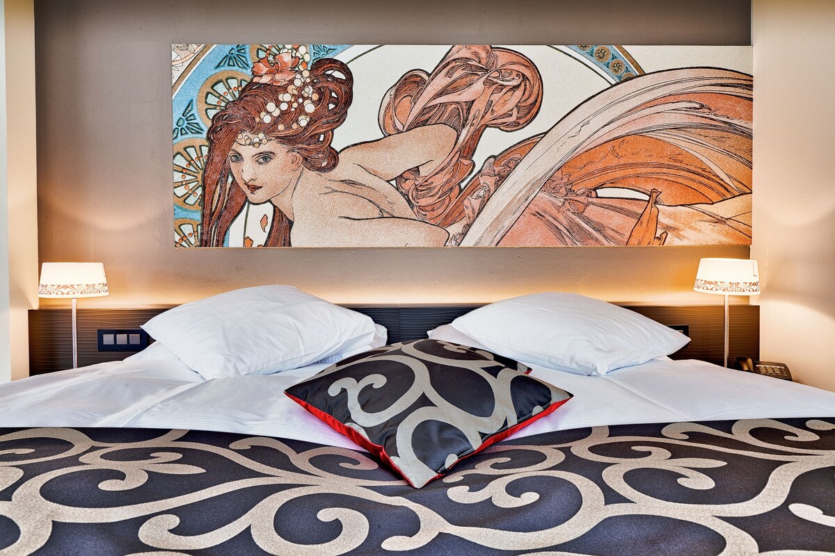 Una habitación de hotel con una cama grande, dos lámparas de noche y una obra de arte grande enmarcada sobre la cama.