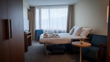 A hotel room with a bed, a desk, a chair, a sofa, and a small table with a vase.