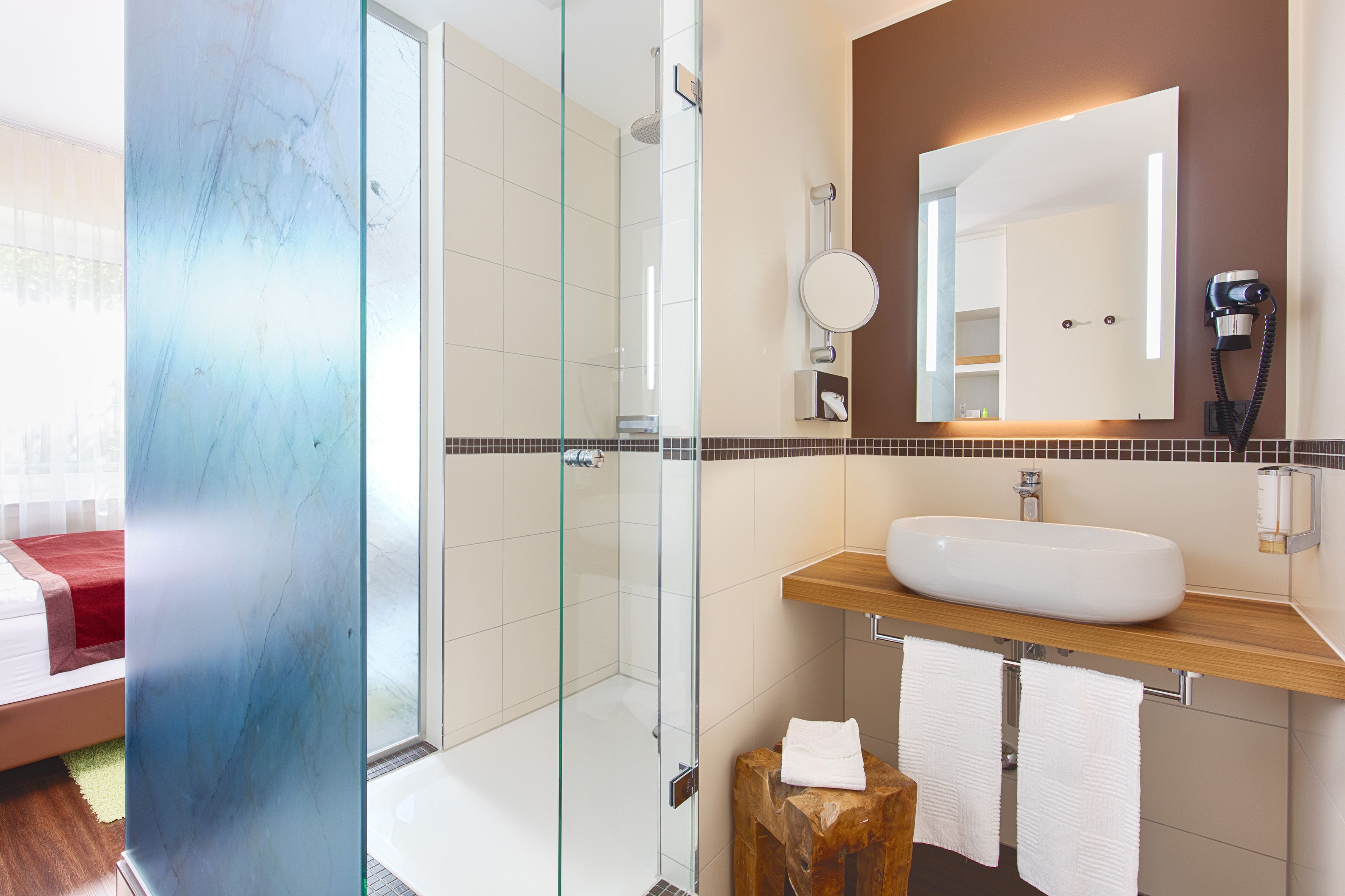 Un baño moderno con ducha envuelta en vidrio, un espejo grande y un tocador de madera con lavabo.