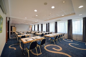 Une salle de conférence équipée de plusieurs tables, de chaises et d’un grand écran.
