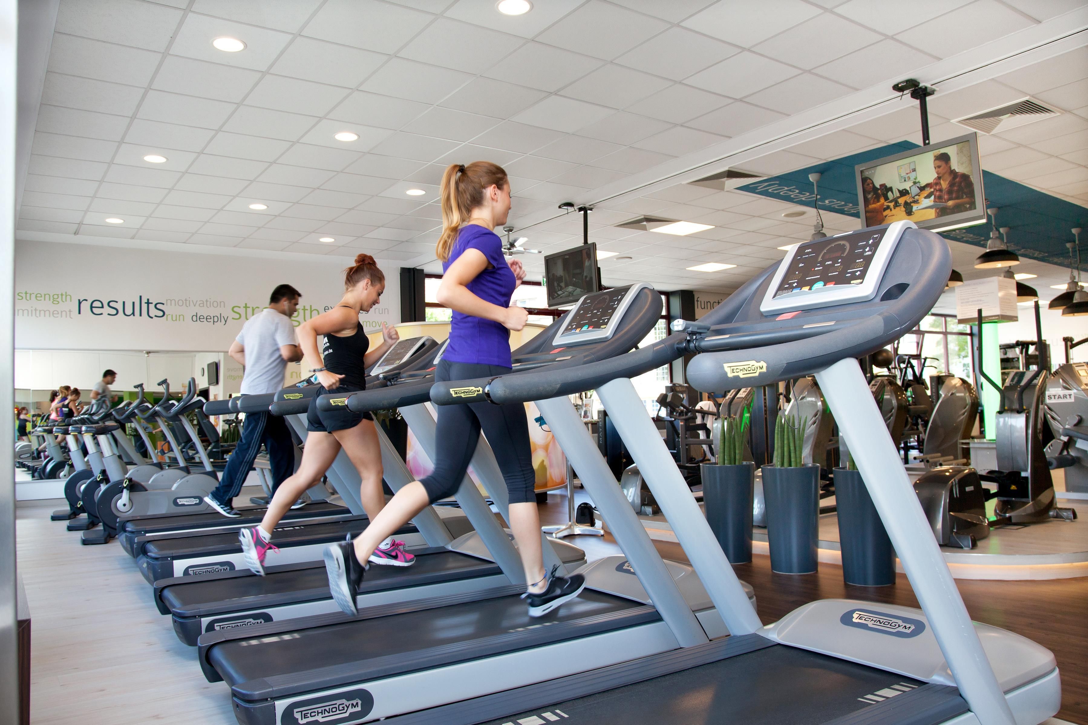 Ein Fitnessstudio mit mehreren Laufbändern, einer Spiegelwand und motivierenden Postern.
