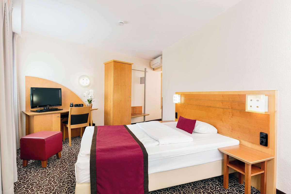 Ein Hotelzimmer mit Bett, Schreibtisch mit Fernseher, Stuhl, kleinem Tisch und Spiegel.