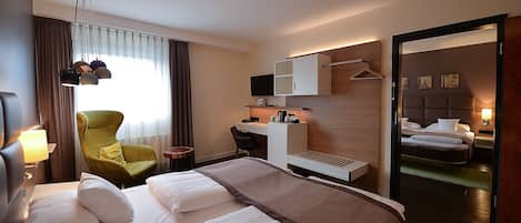 A hotel room with a large bed, a desk with a computer, a chair, and a mirror.