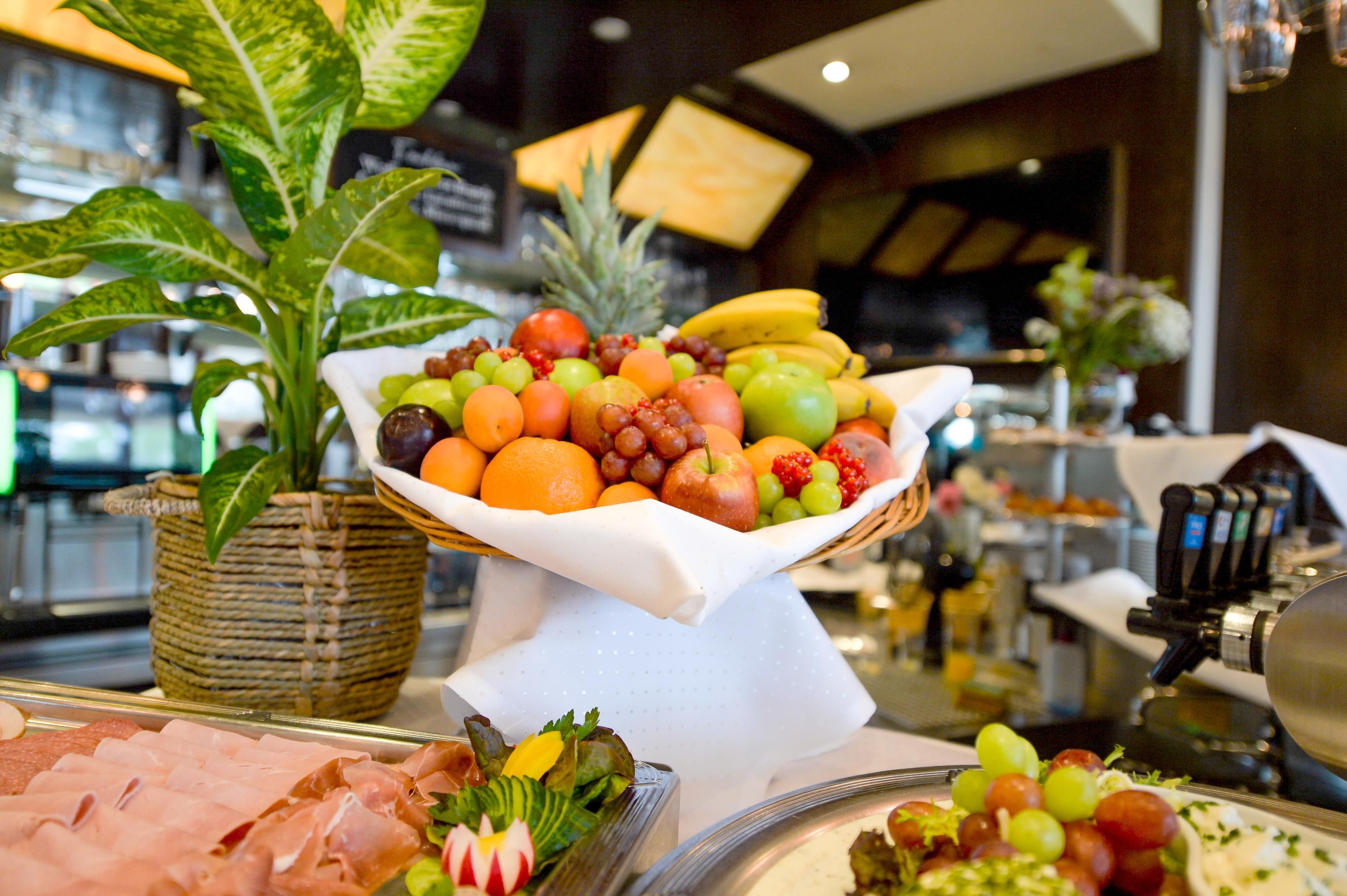 Ein Buffet mit verschiedenen Früchten und Gemüsesorten, darunter Äpfel, Orangen und Weintrauben, auf einem weißen Tisch arrangiert.