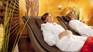 Two reclining chairs in a spa setting with a warm-toned wall and plants.