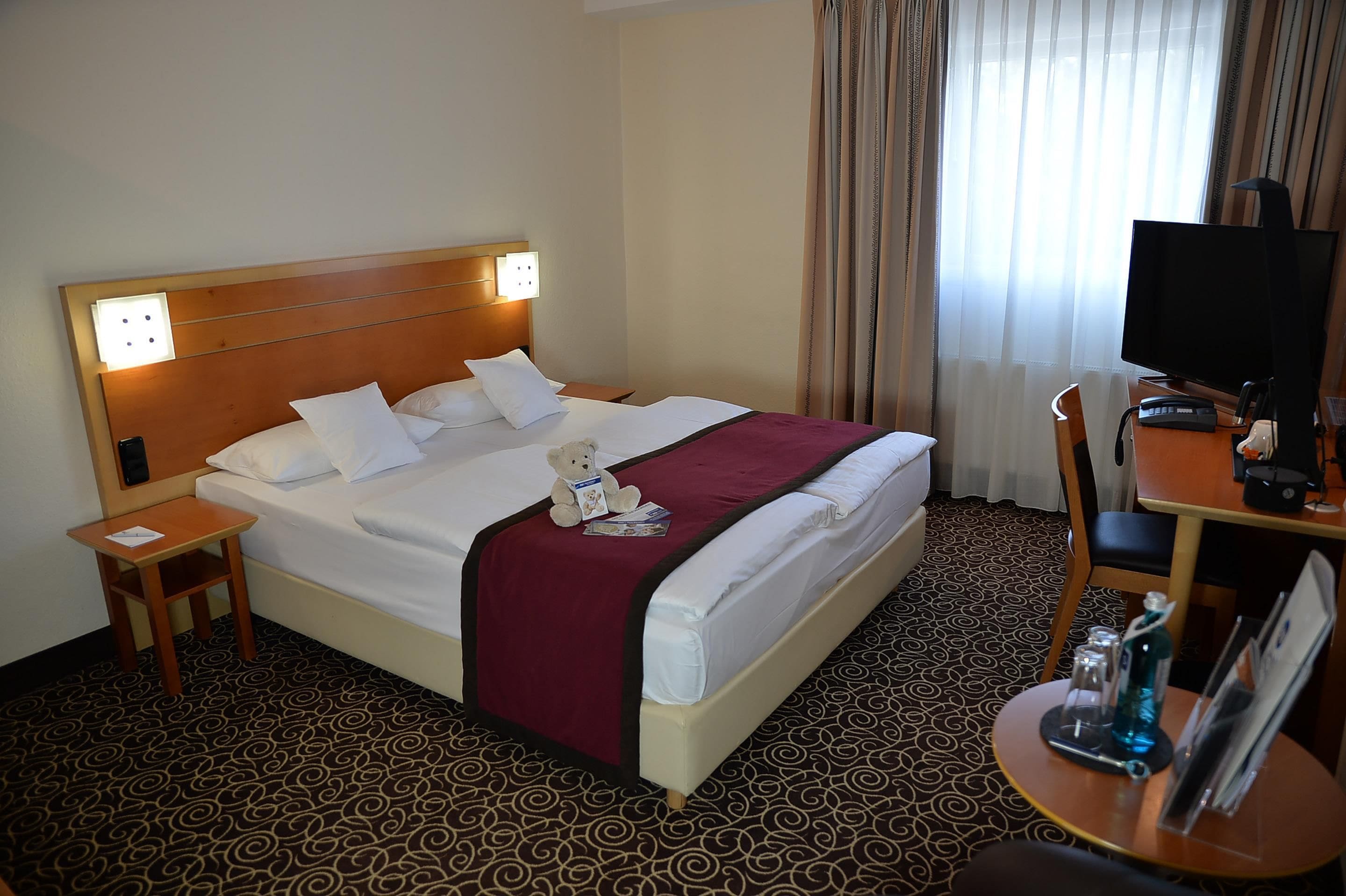 A hotel room with a bed, a desk with a television, and a chair.