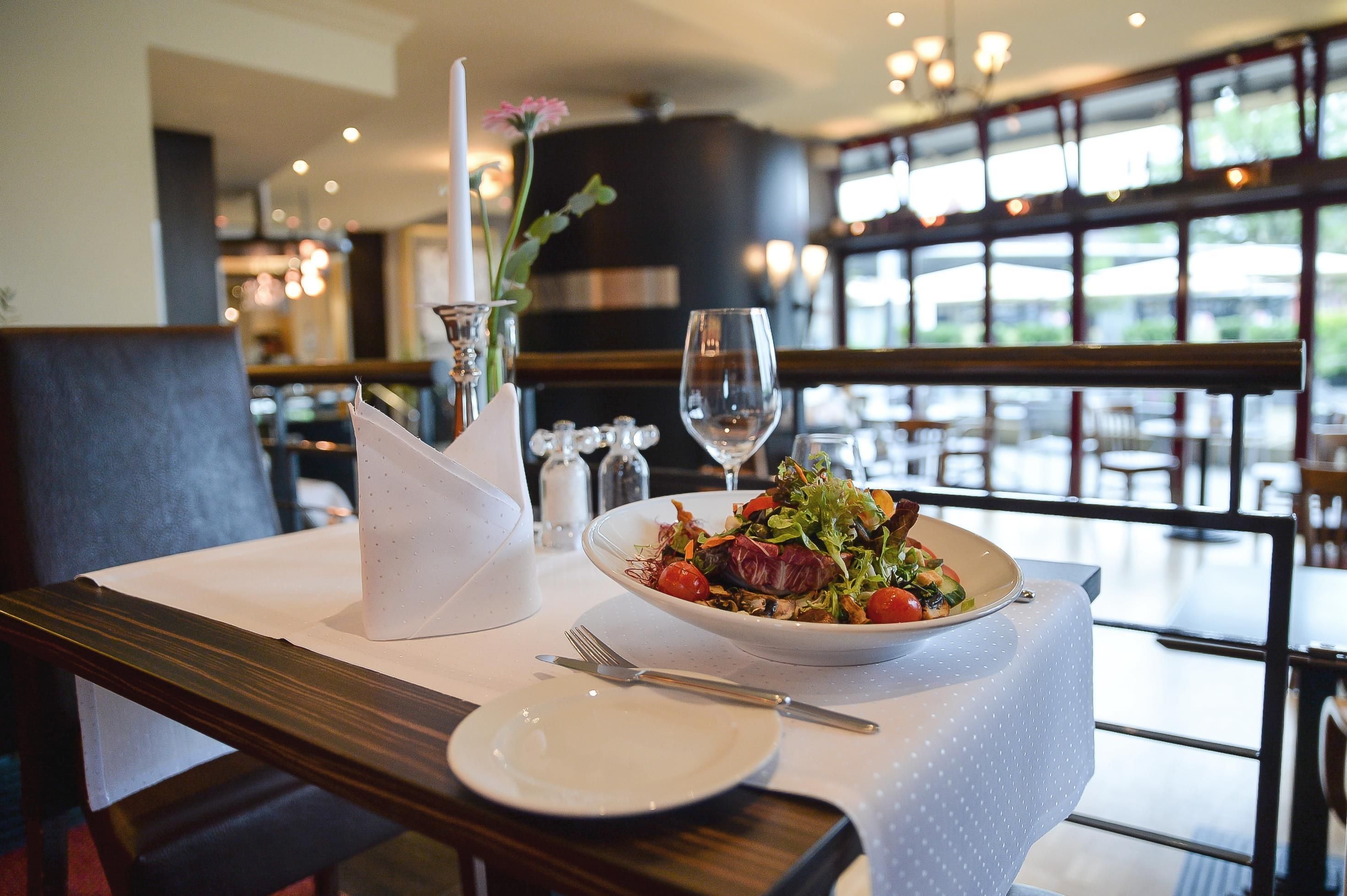 Une table à manger avec une salade, un verre à vin et des couverts.