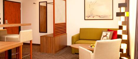 A modern hotel room with a dining area, a sofa, and a painting on the wall.