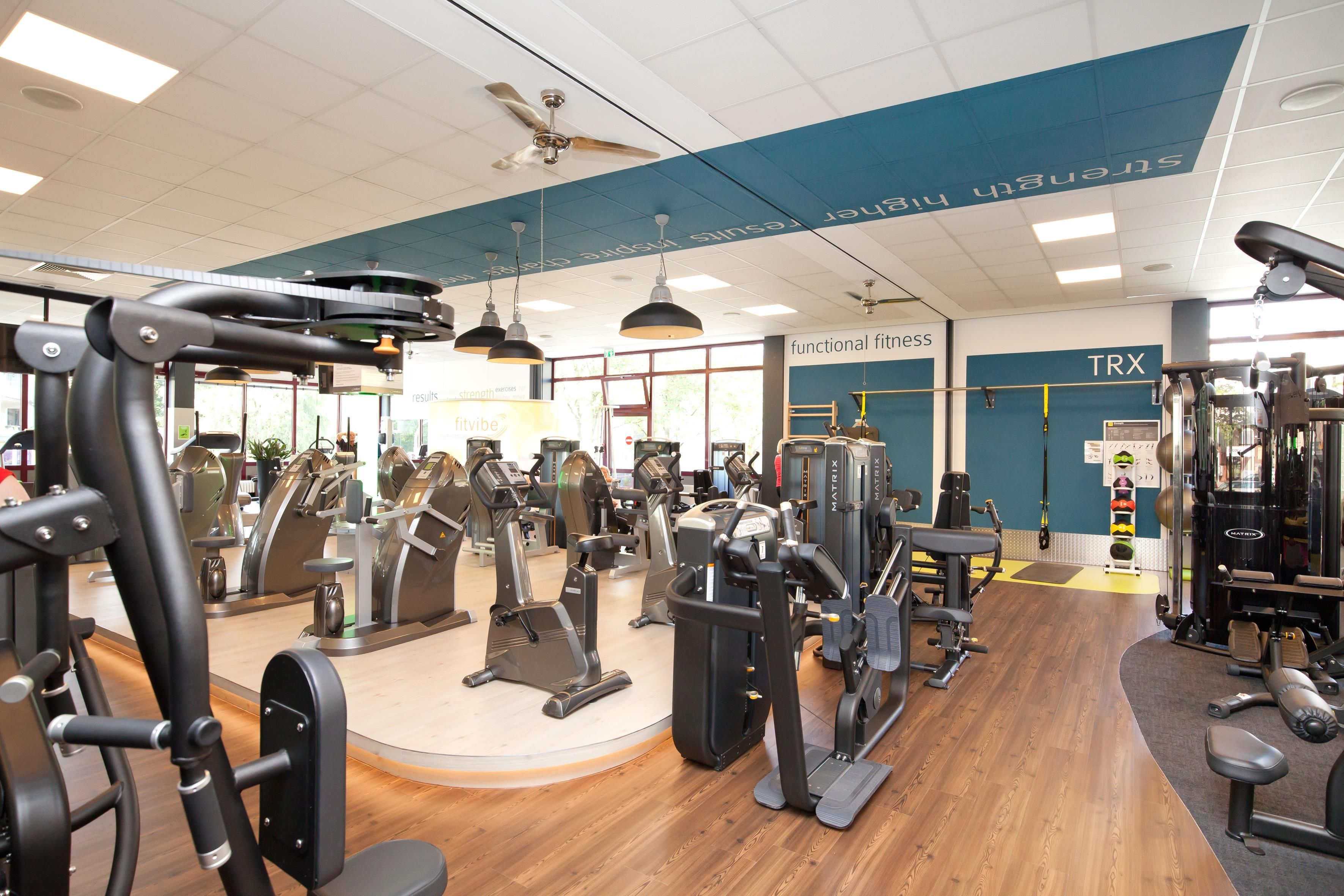 Un gimnasio con diferentes máquinas de ejercicio, incluyendo cintas de correr, equipos de pesas y pesas libres.