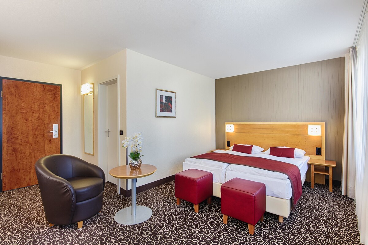 A hotel room with a bed, a chair, a small table, and a mirror.
