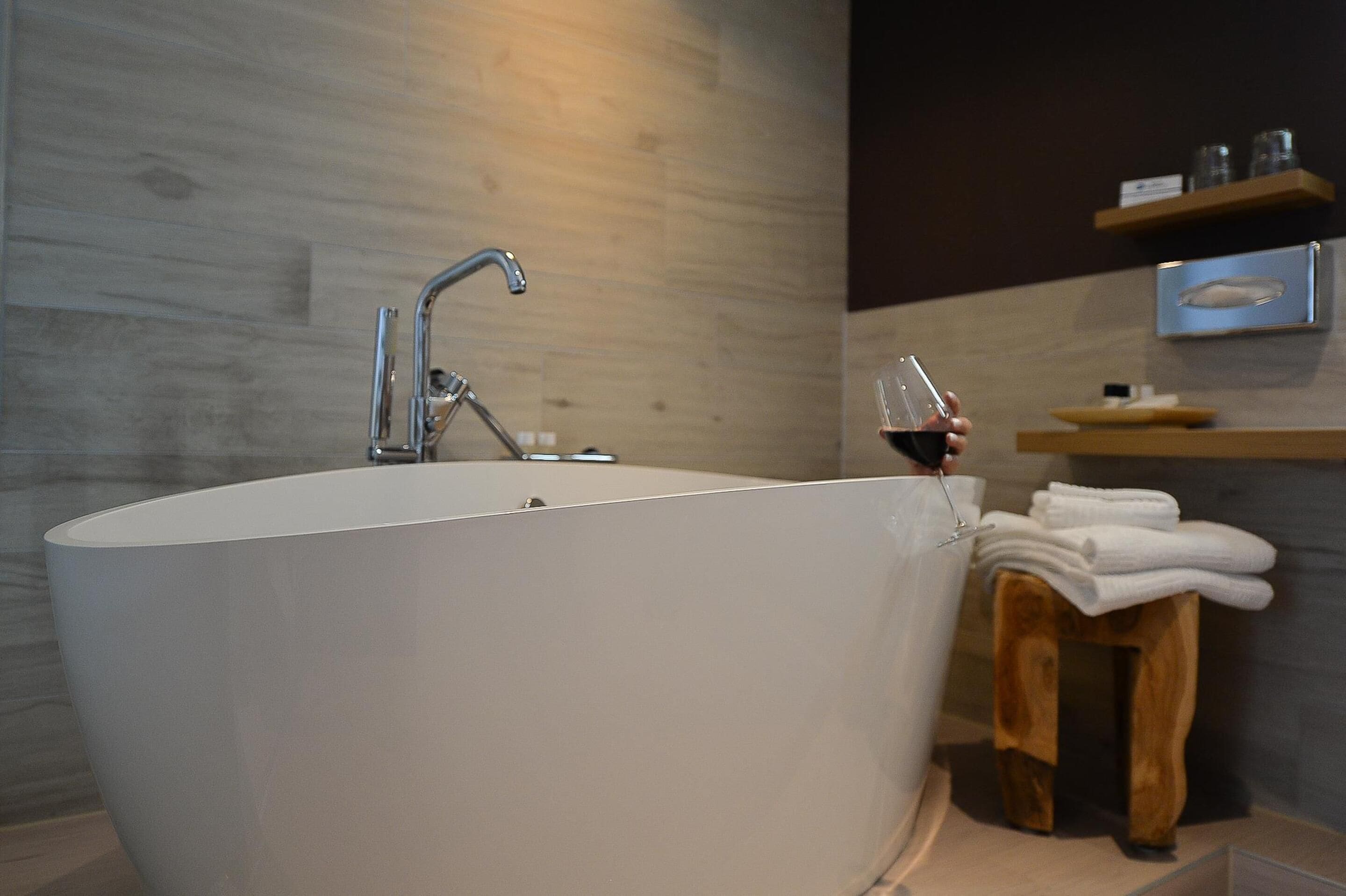 A modern bathroom with a freestanding bathtub, a wooden stool with towels, and a shelf with toiletries.