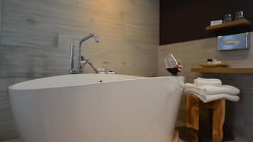 A modern bathroom with a freestanding bathtub, a wooden stool with towels, and a shelf with toiletries.