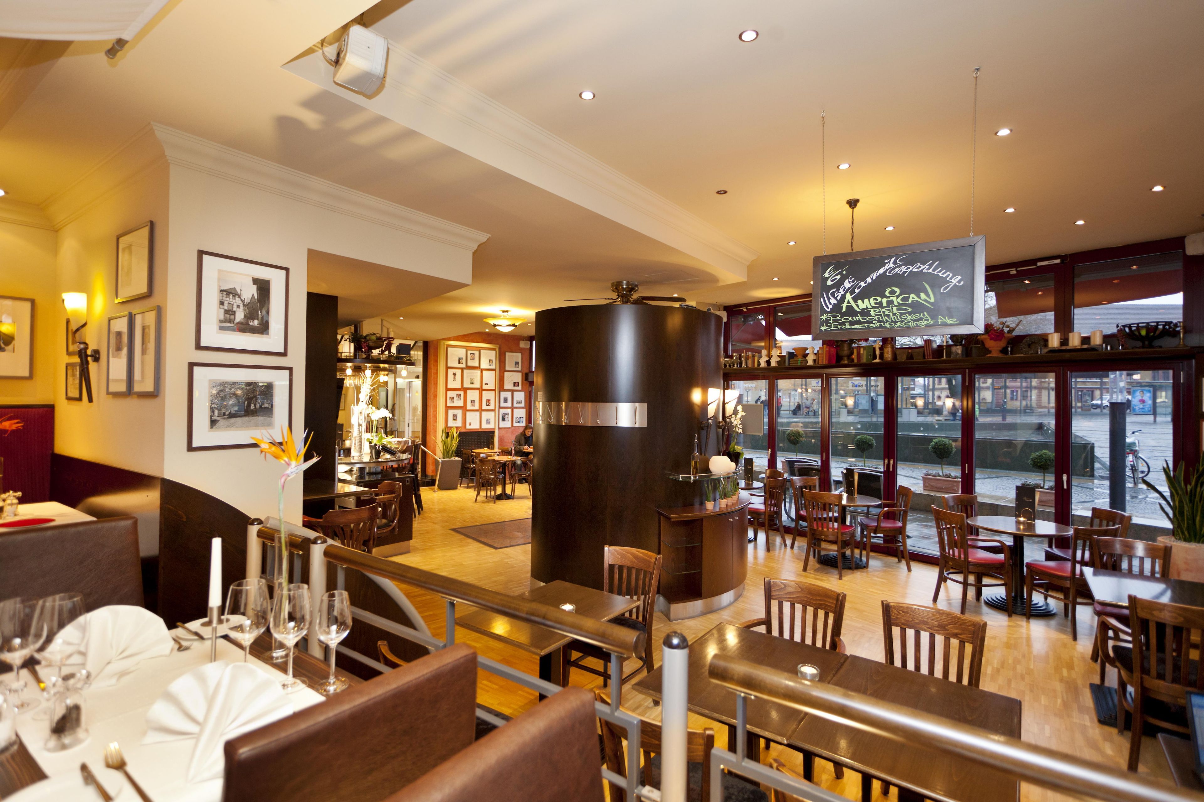 A restaurant with a bar area, wooden furniture, and a view through large windows.