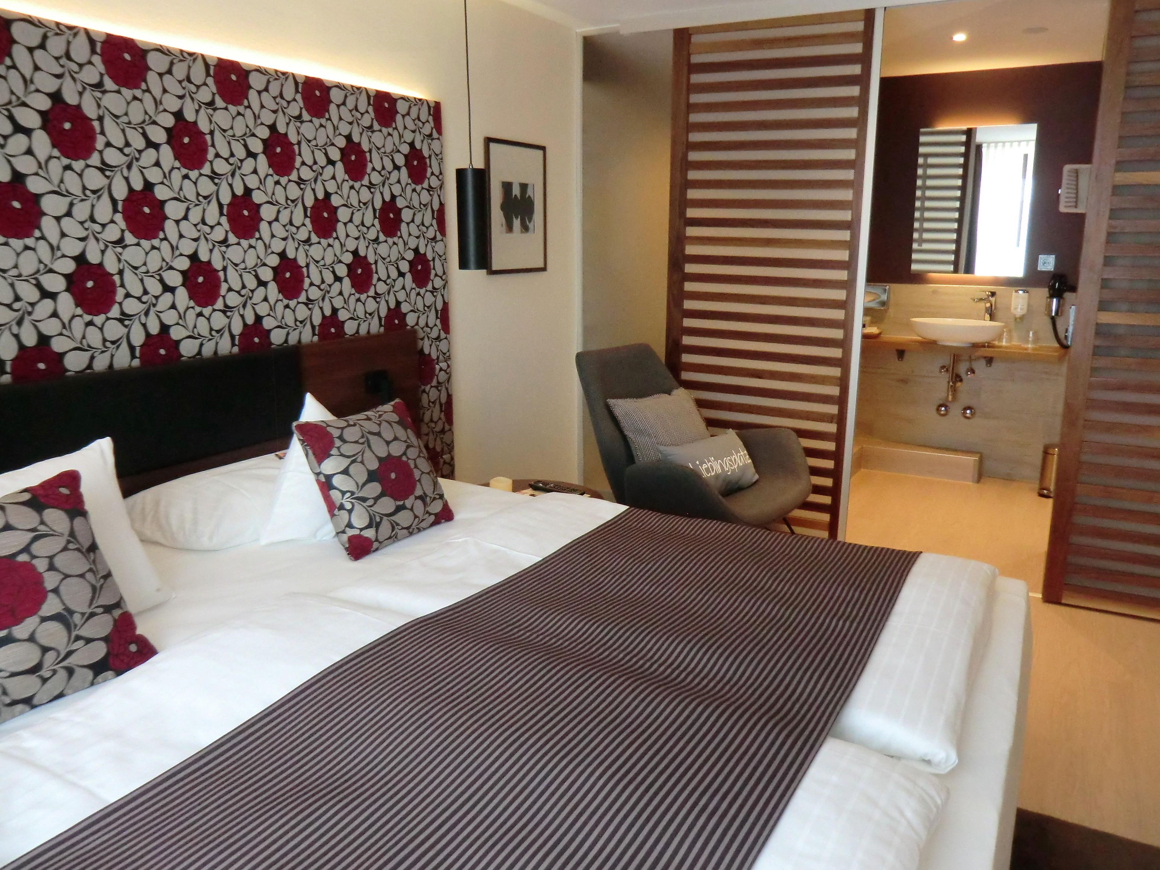 Ein Hotelzimmer mit Bett, Sessel, Badezimmer mit Waschbecken und Spiegel.