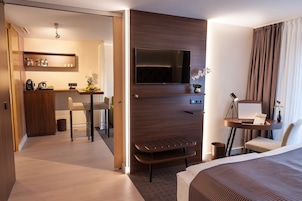 A modern hotel room with a flat-screen TV, a desk with a laptop, a chair, a bed, and a small seating area.