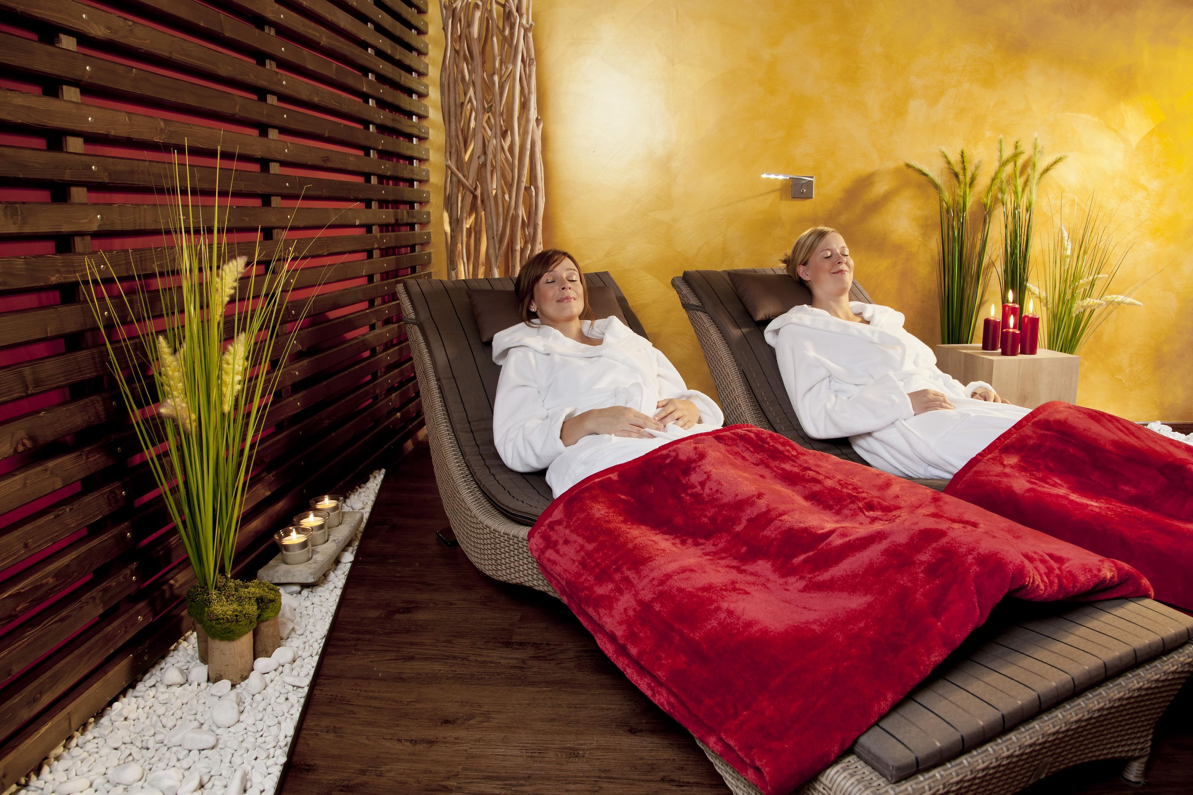 Dos sillones reclinables con una manta roja, una pared de listones de madera y una planta con hierba alta.