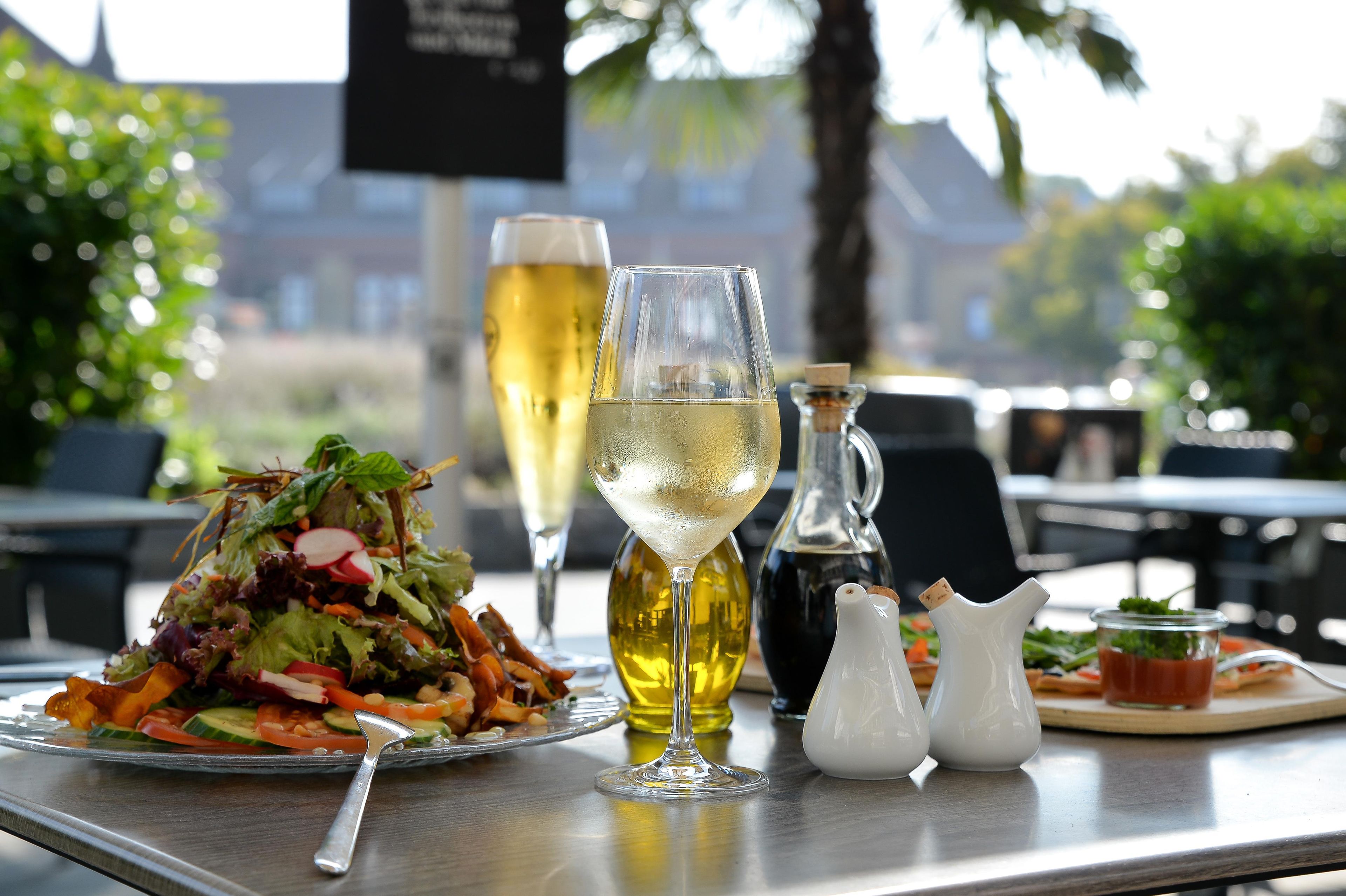 Een tafel met een salade, een glas witte wijn, een fles olijfolie en zout- en peperstrooiers.