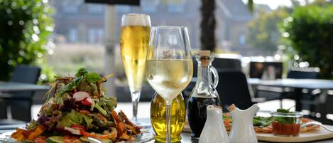 A table with a salad, a glass of white wine, a bottle of olive oil, and salt and pepper shakers.