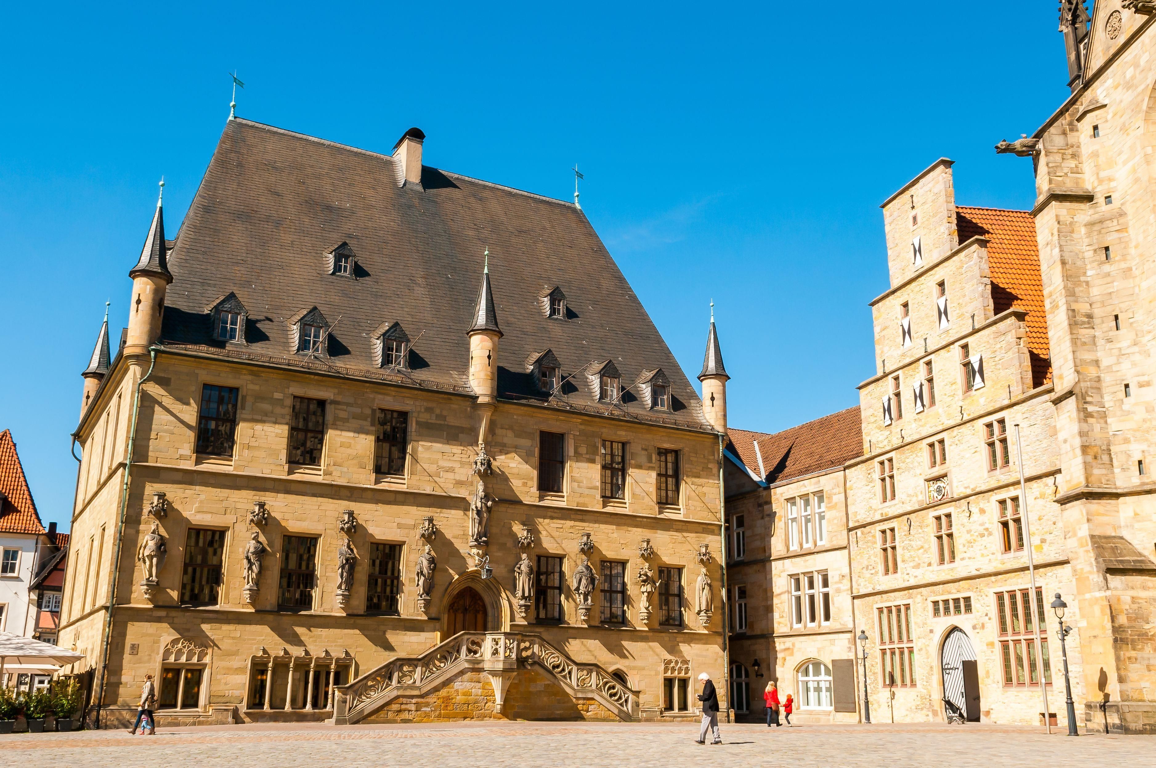 A historic building with a prominent entrance, a staircase leading up to the main entrance, and a clear blue sky in the background.