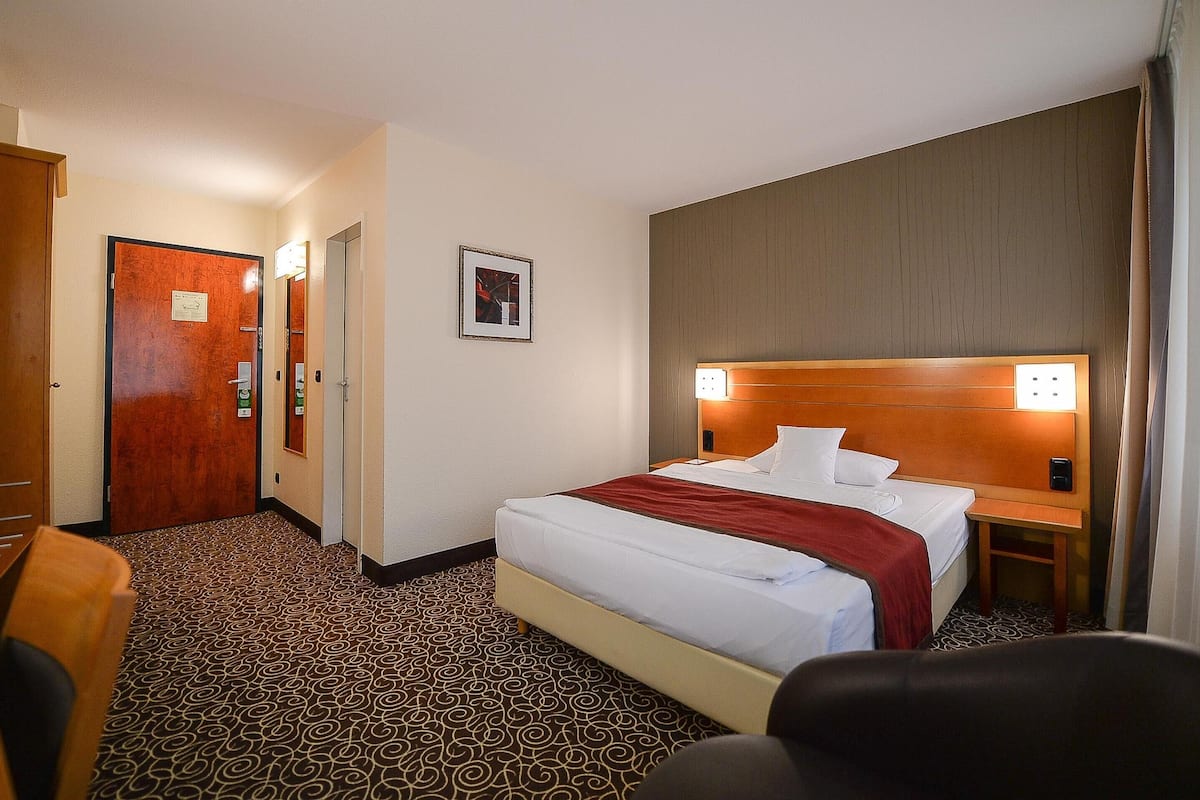 Ein Hotelzimmer mit einem großen Bett, einem Nachttisch, einem Spiegel und einer Tür zu einem Flur.