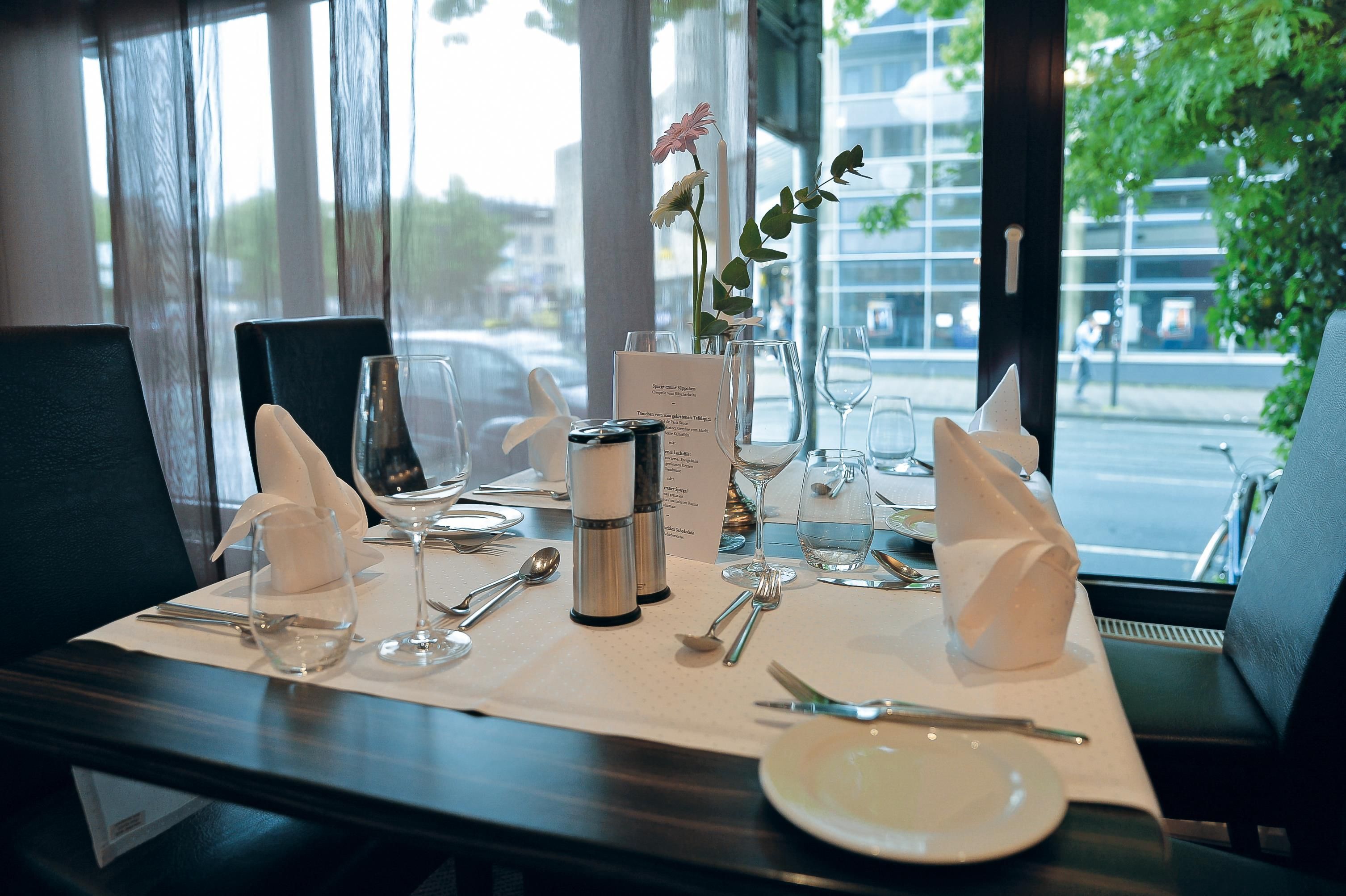 A table set for dining with a menu, glasses, cutlery, and a vase with flowers.