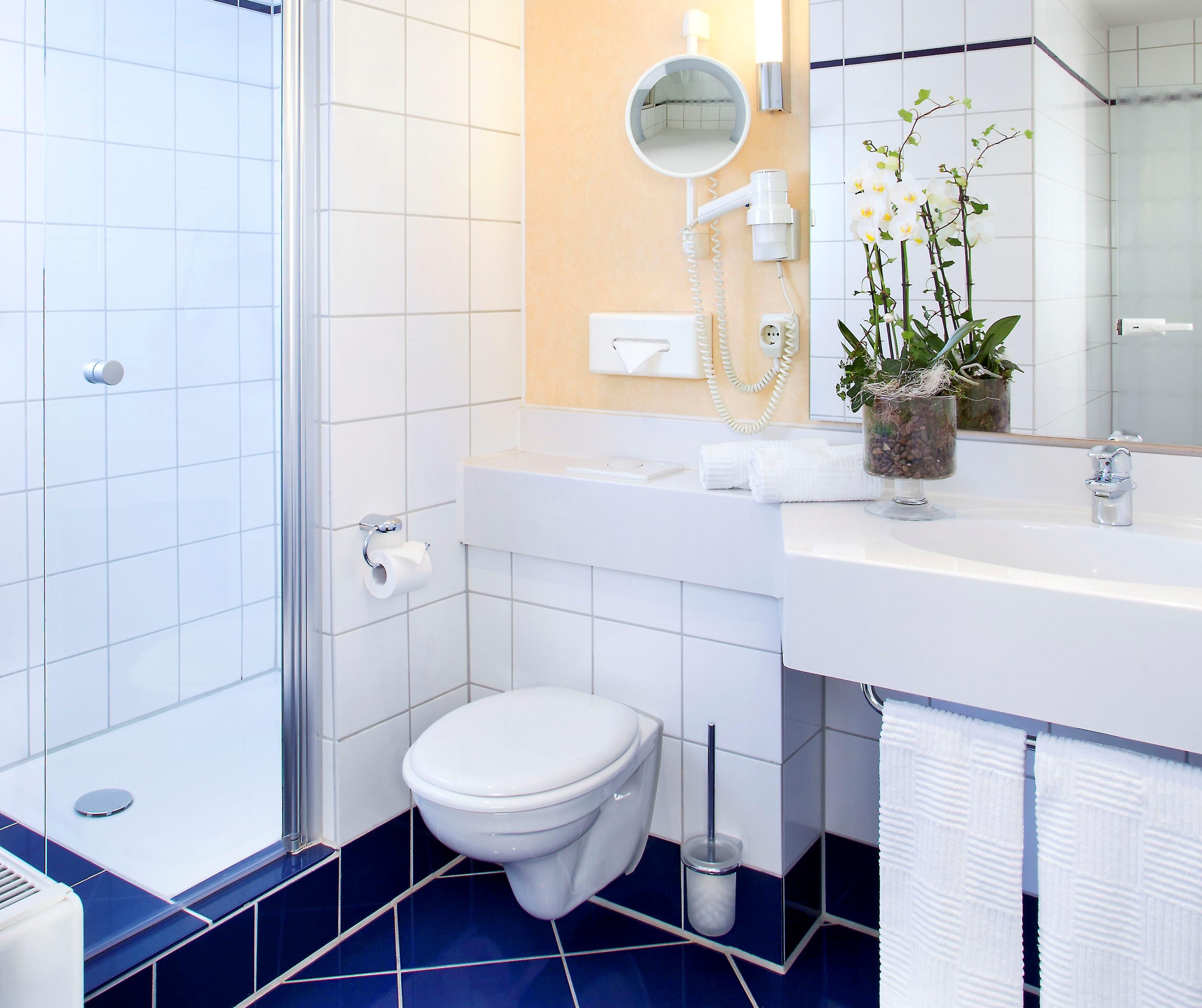 A bathroom with a toilet, sink, mirror, and a potted plant.