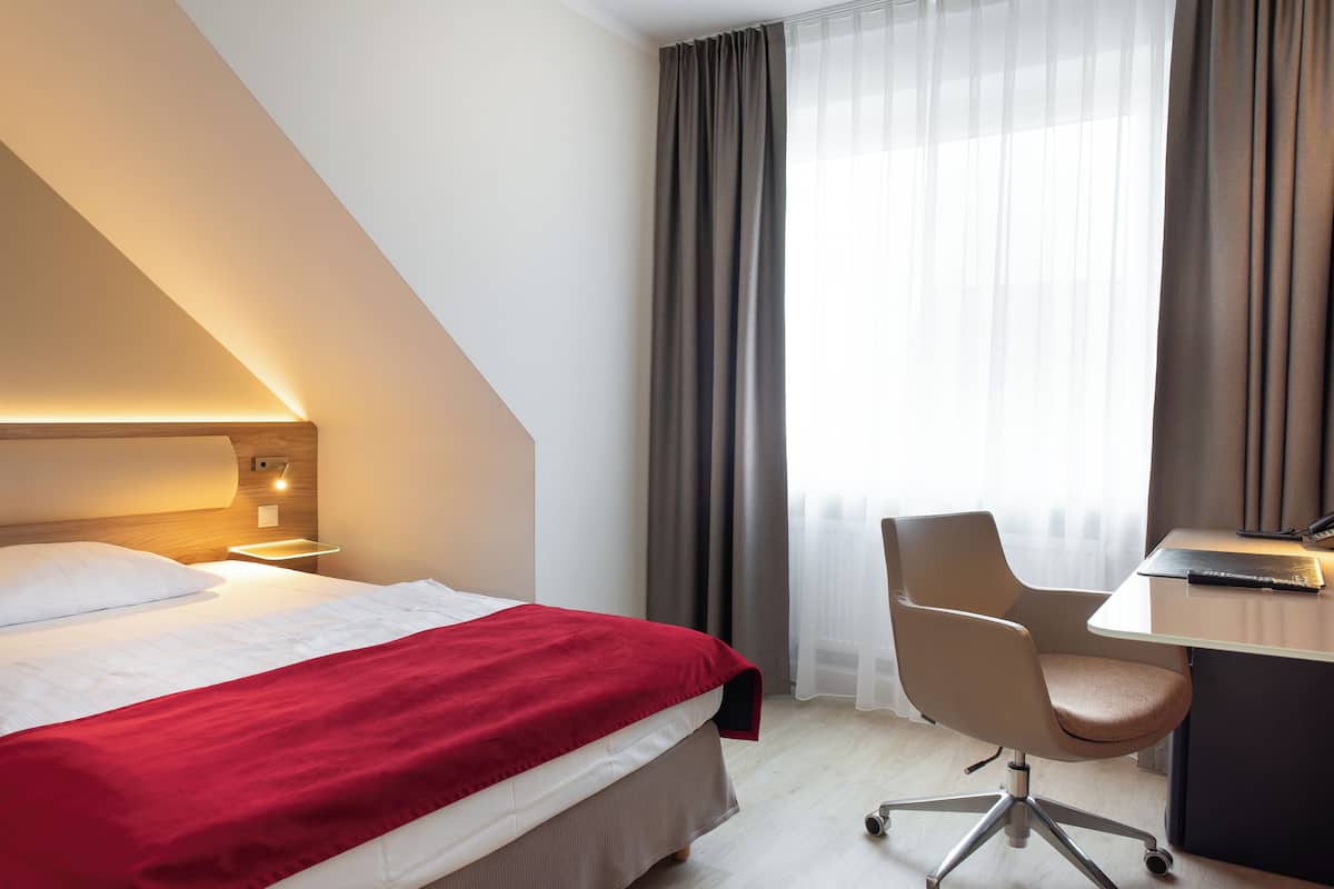 Ein Hotelzimmer mit Bett, Schreibtisch, Stuhl und einem Fenster mit Vorhängen.