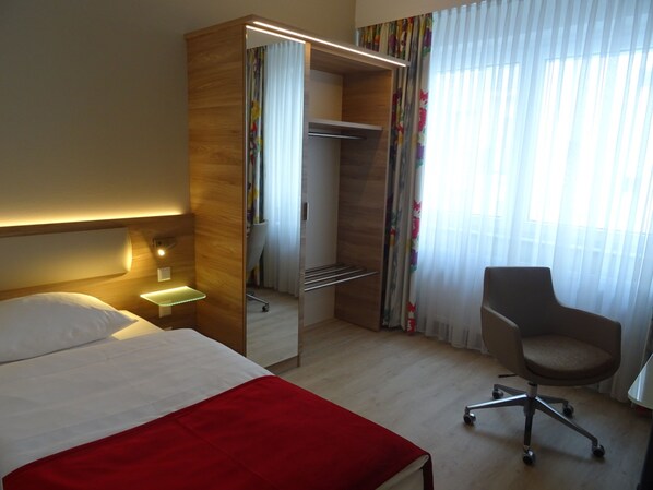 Una habitación de hotel con cama, escritorio, silla y armario.