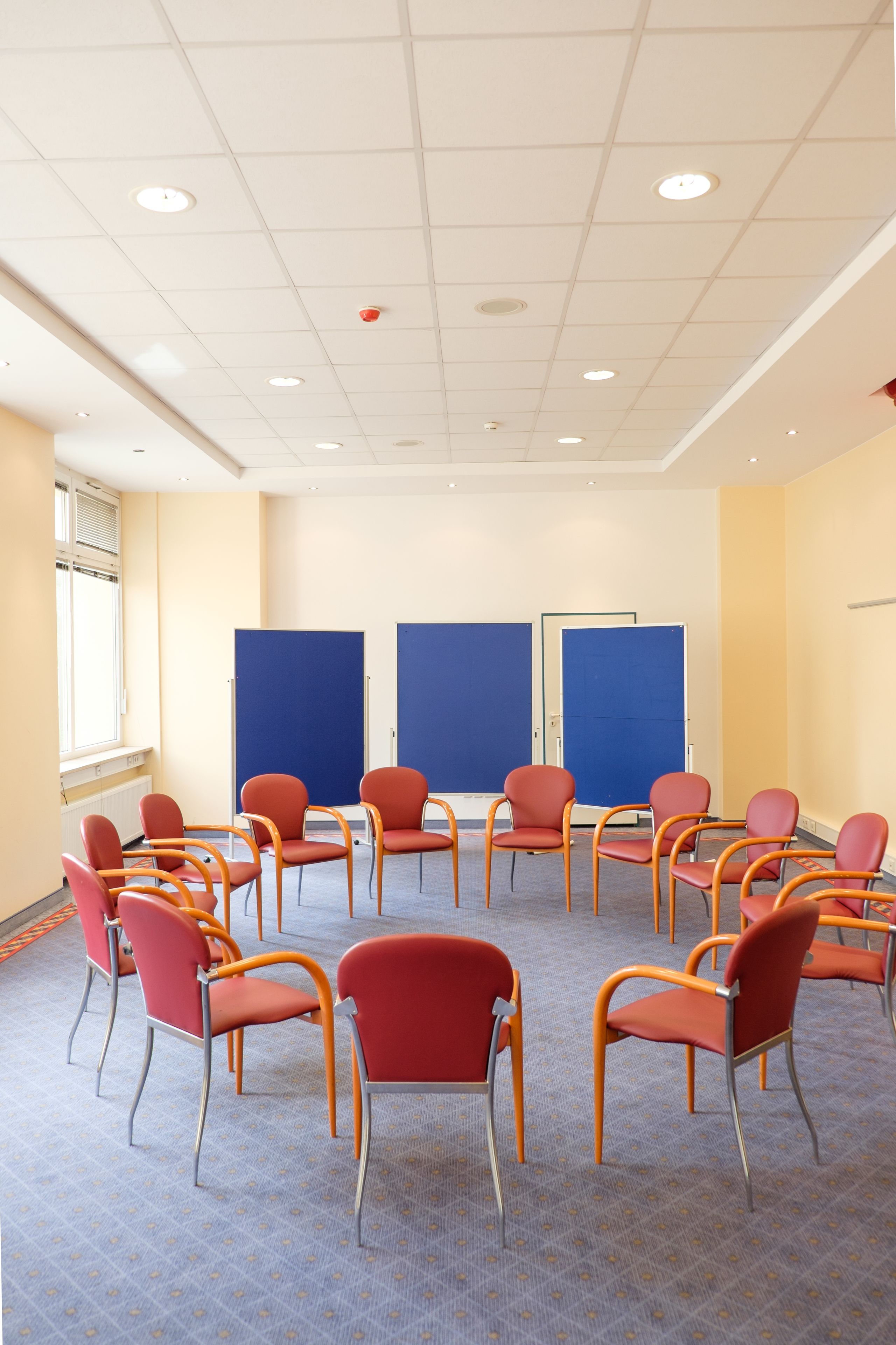 A conference room with rows of red chairs, a white ceiling, and a large window on the left.