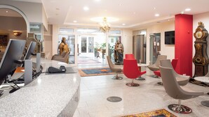 A modern hotel lobby with a reception desk, comfortable seating, a chandelier, and a statue.