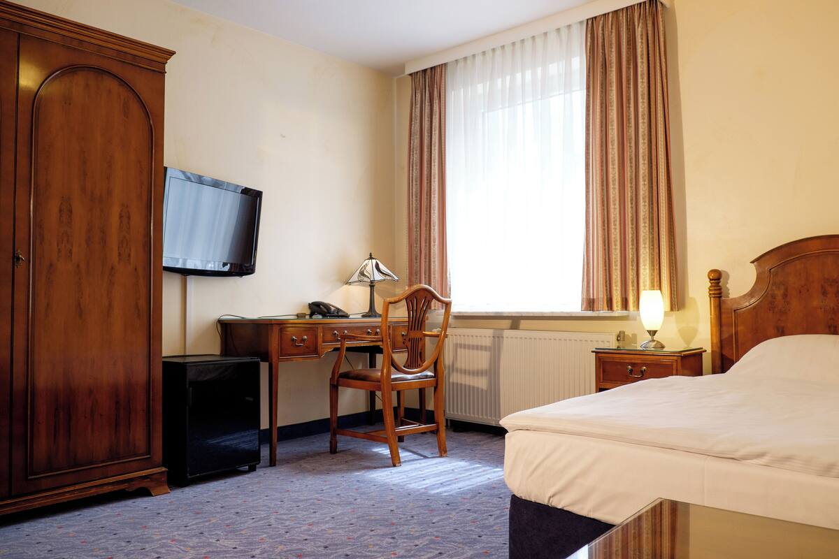 Ein Hotelzimmer mit einem Bett, einem Schreibtisch mit Stuhl, einem Fernseher und einem fenster mit Vorhängen.
