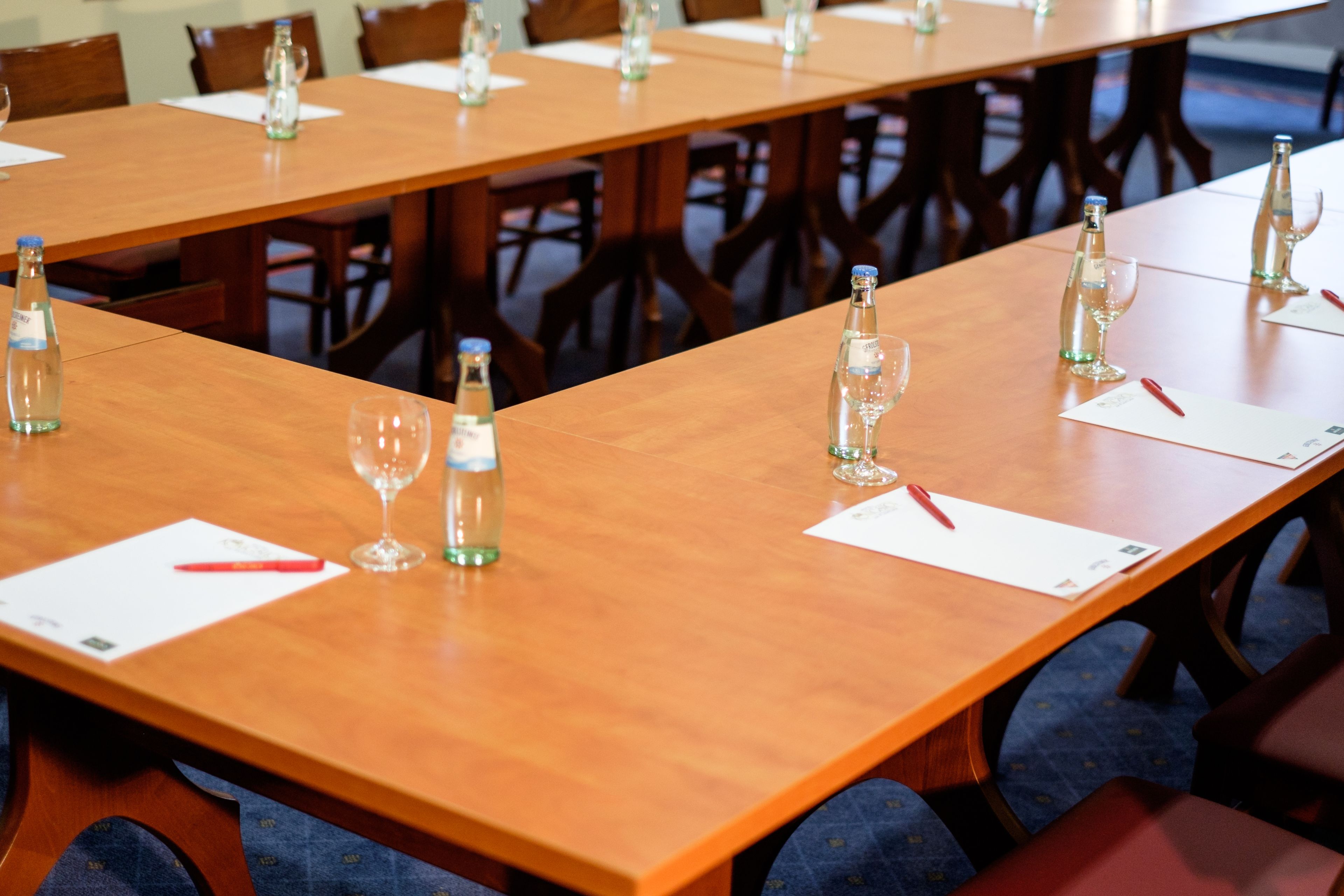 Un salón de conferencias con largas mesas, sillas, botellas de agua y vasos.