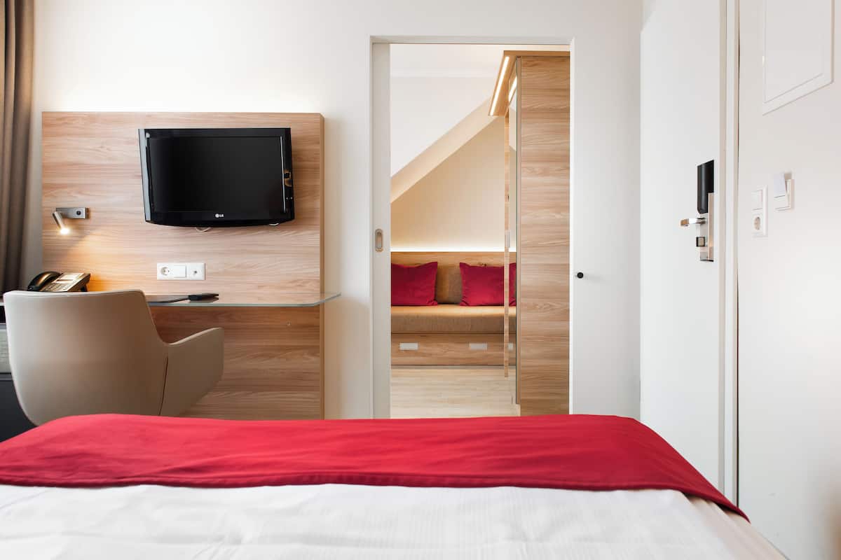 Ein Hotelzimmer mit einem Bett, einem Schreibtisch mit Stuhl, einem an der Wand befestigten Fernseher und einer Treppe zu einem Schlafbereich mit einer Couch.