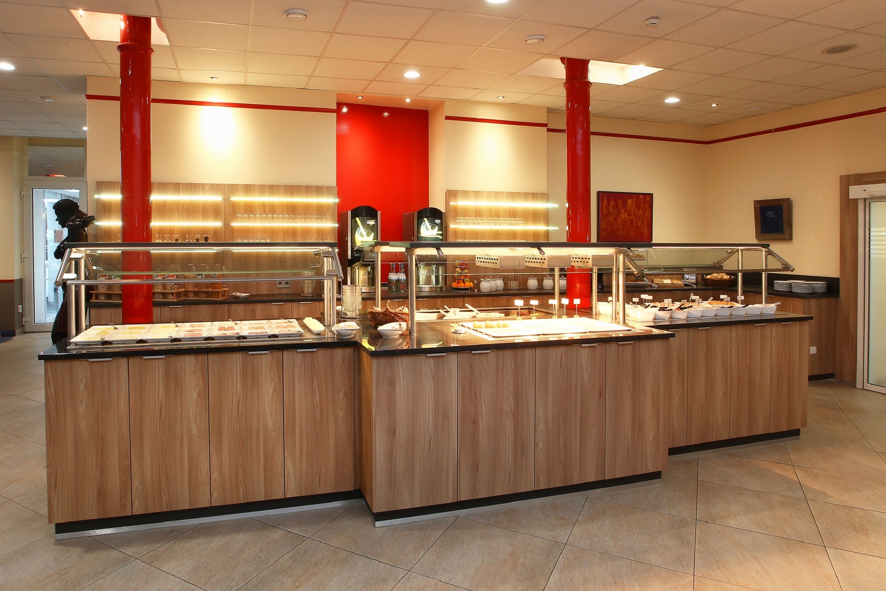 A buffet area with multiple serving stations, a red accent wall, and a tiled floor.
