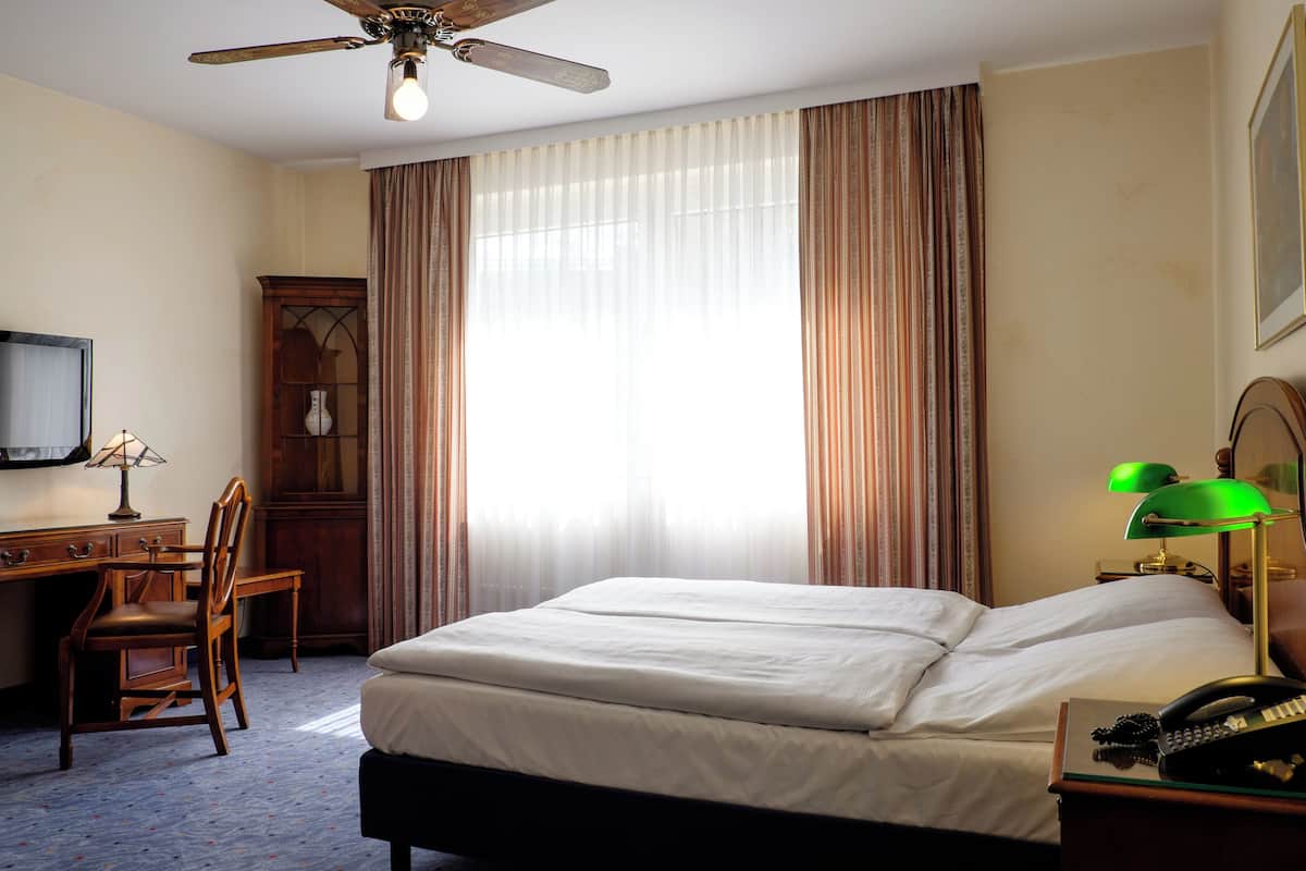 Ein Hotelzimmer mit einem Bett, einem Schreibtisch, einem Sessel, einem Telefon und einem Fernseher.