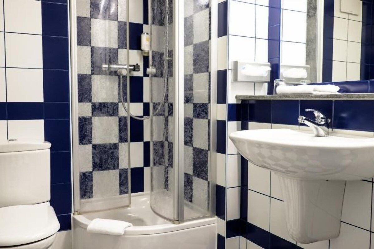 A bathroom with a checkered tile pattern, a glass shower enclosure, a white sink, and a toilet.